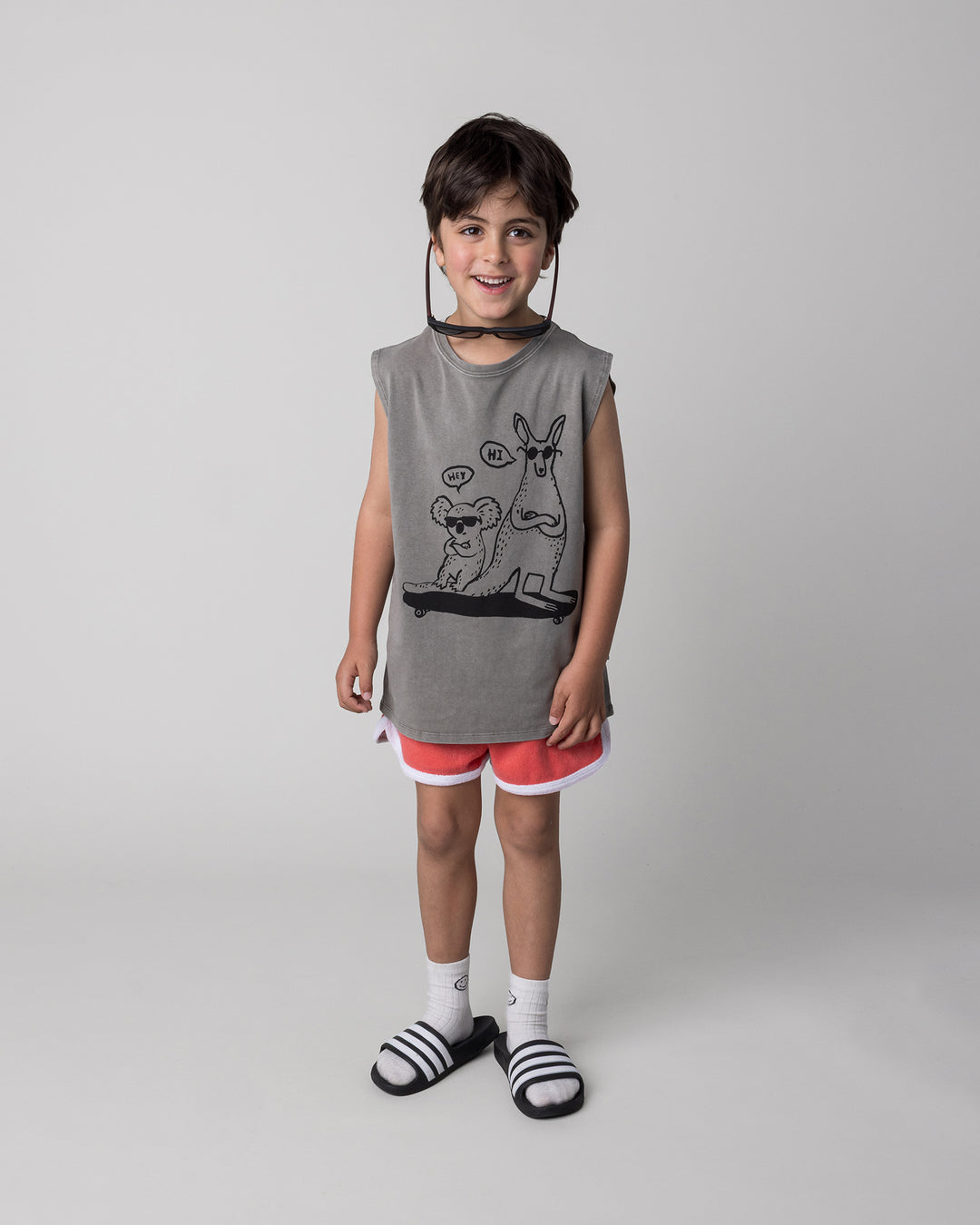 Kid wearing the Chill Mates Sleeveless Tee in grey wash with the Track Star Short in tangerine, front view