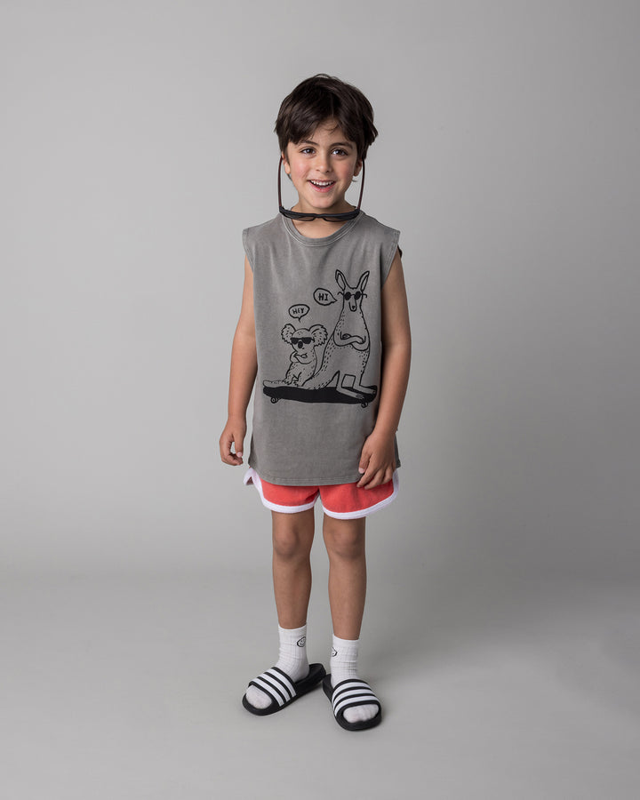 Kid wearing the Chill Mates Sleeveless Tee in grey wash with the Track Star Short in tangerine, front view