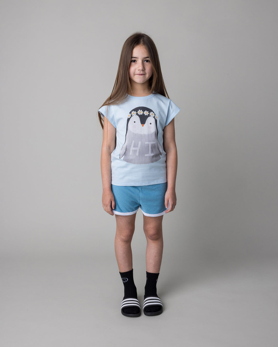 Kid wearing the Flower Penguin Tee in light blue with the Track Star Short in ocean, front view