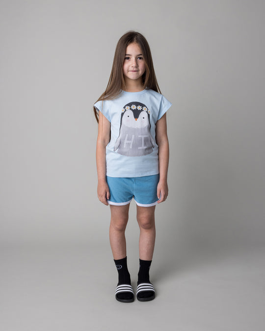 Kid wearing the Flower Penguin Tee in light blue with the Track Star Short in ocean, front view