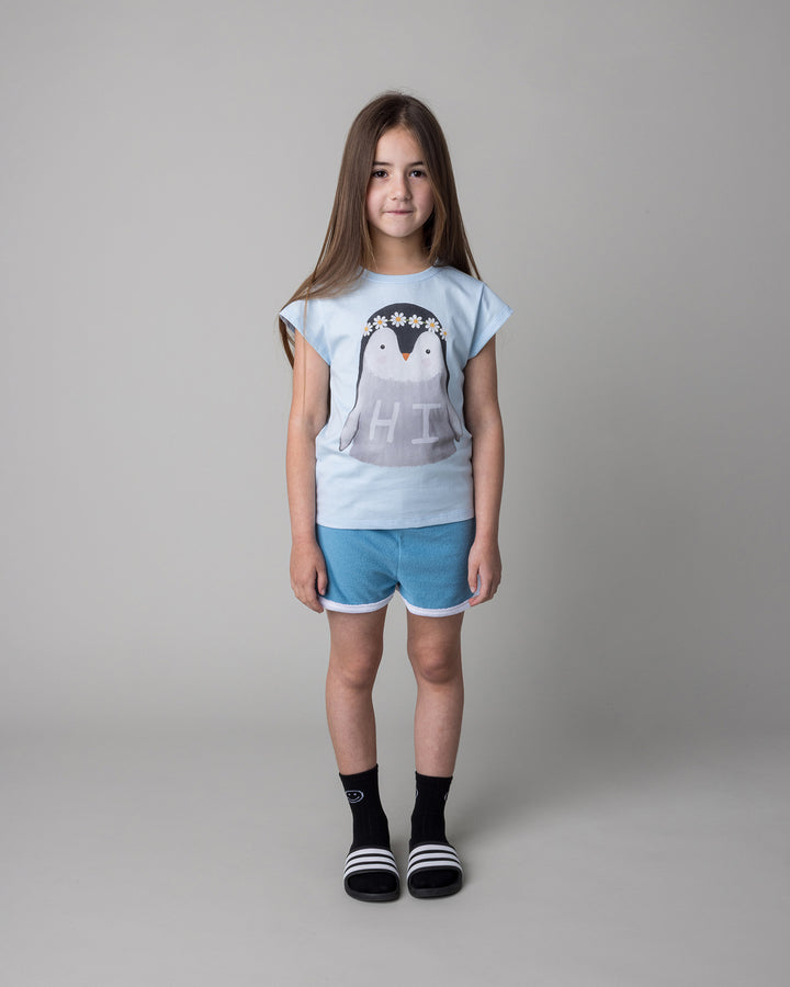 Kid wearing the Flower Penguin Tee in light blue with the Track Star Short in ocean, front view