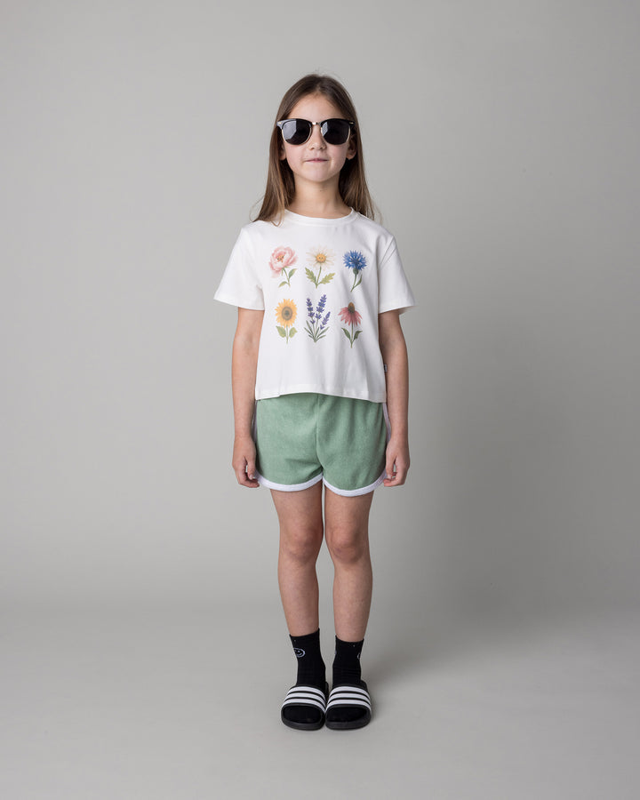 Kid wearing the Track Star Short in sage with the Flower Friends Cropped Tee in white, front view