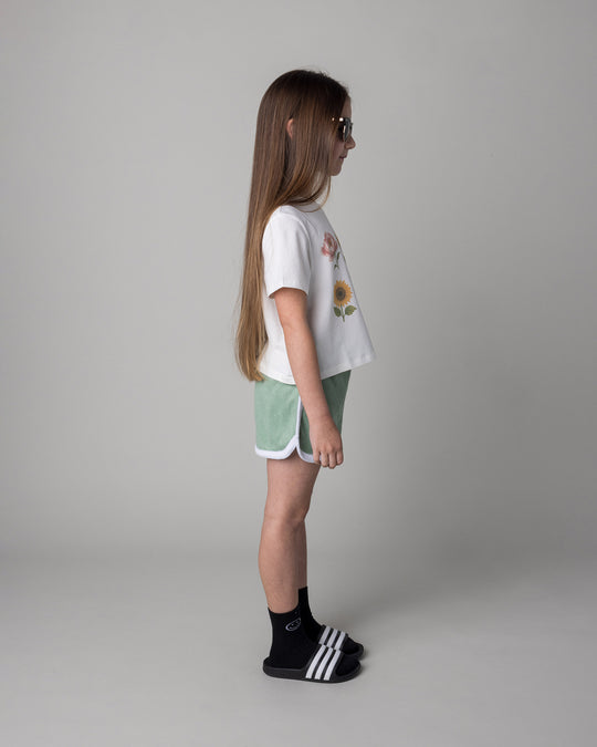 Kid wearing the Track Star Short in sage with the Flower Friends Cropped Tee in white, side view