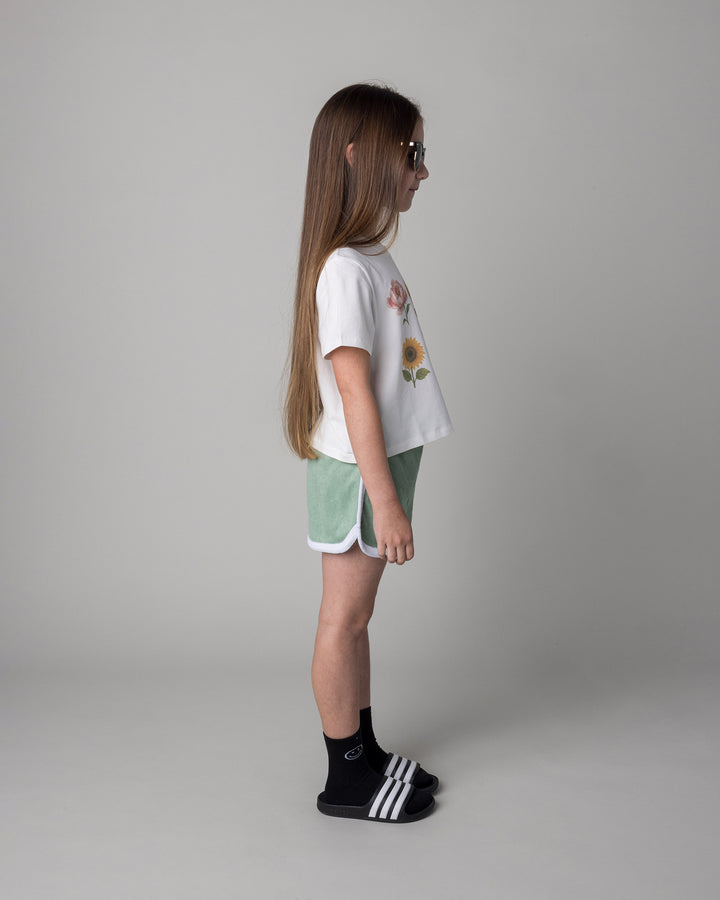 Kid wearing the Track Star Short in sage with the Flower Friends Cropped Tee in white, side view