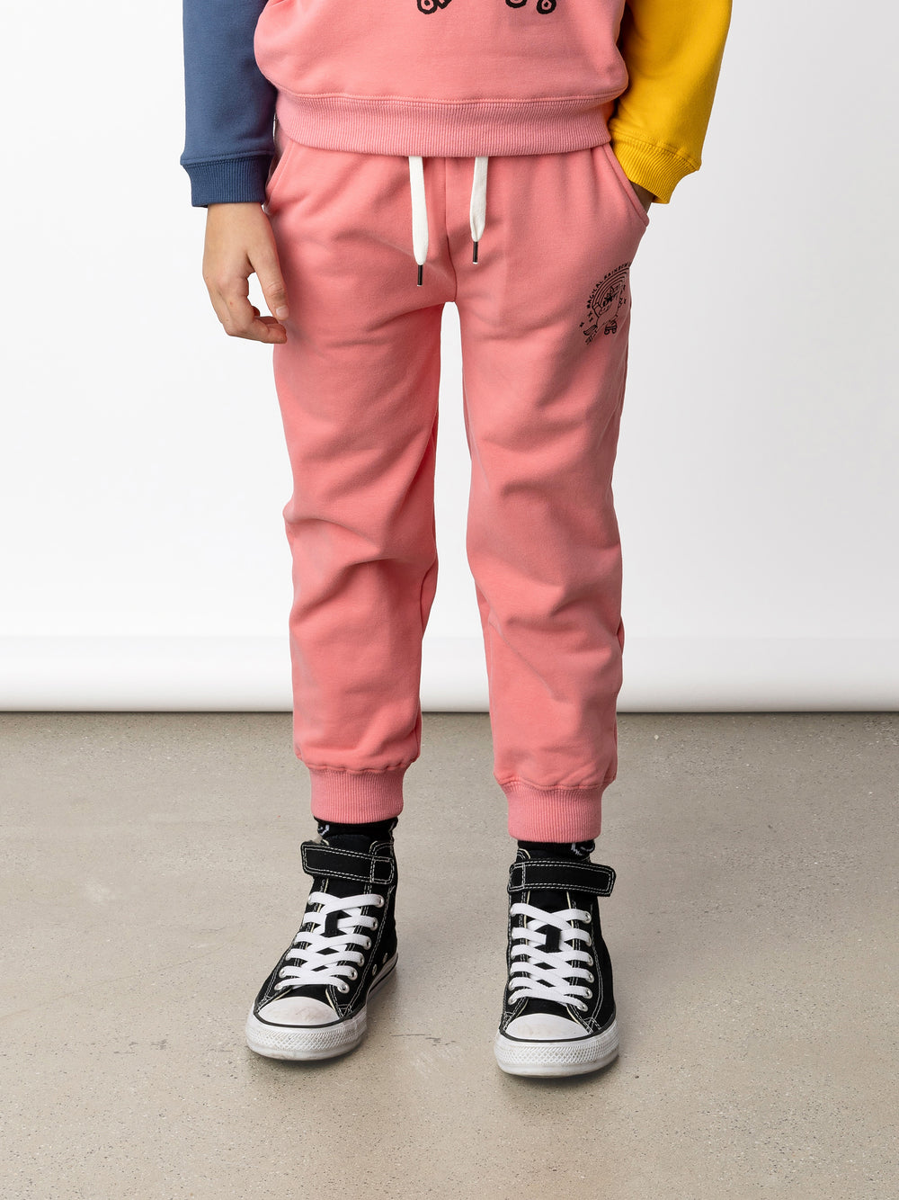 Minti kids clothing. Relaxed fit trackies with cosy side pockets, elasticated waistband, shoelace cord and 2x2 Rib cuffs. Small Magical Rainbow Unicorn print on the front. 330 Gram // Brushed Inside // 95% Cotton // 5% Elastane.