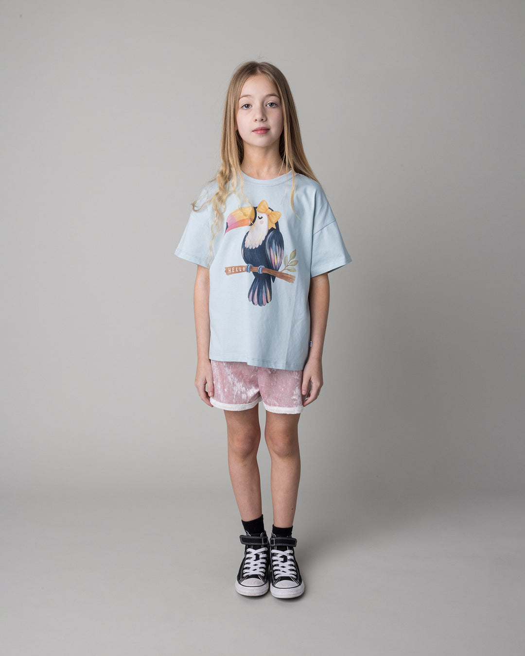 Kid wearing the Hello Toucan Tee in light blue with the Velvet Runner Short in blush and cream, front view
