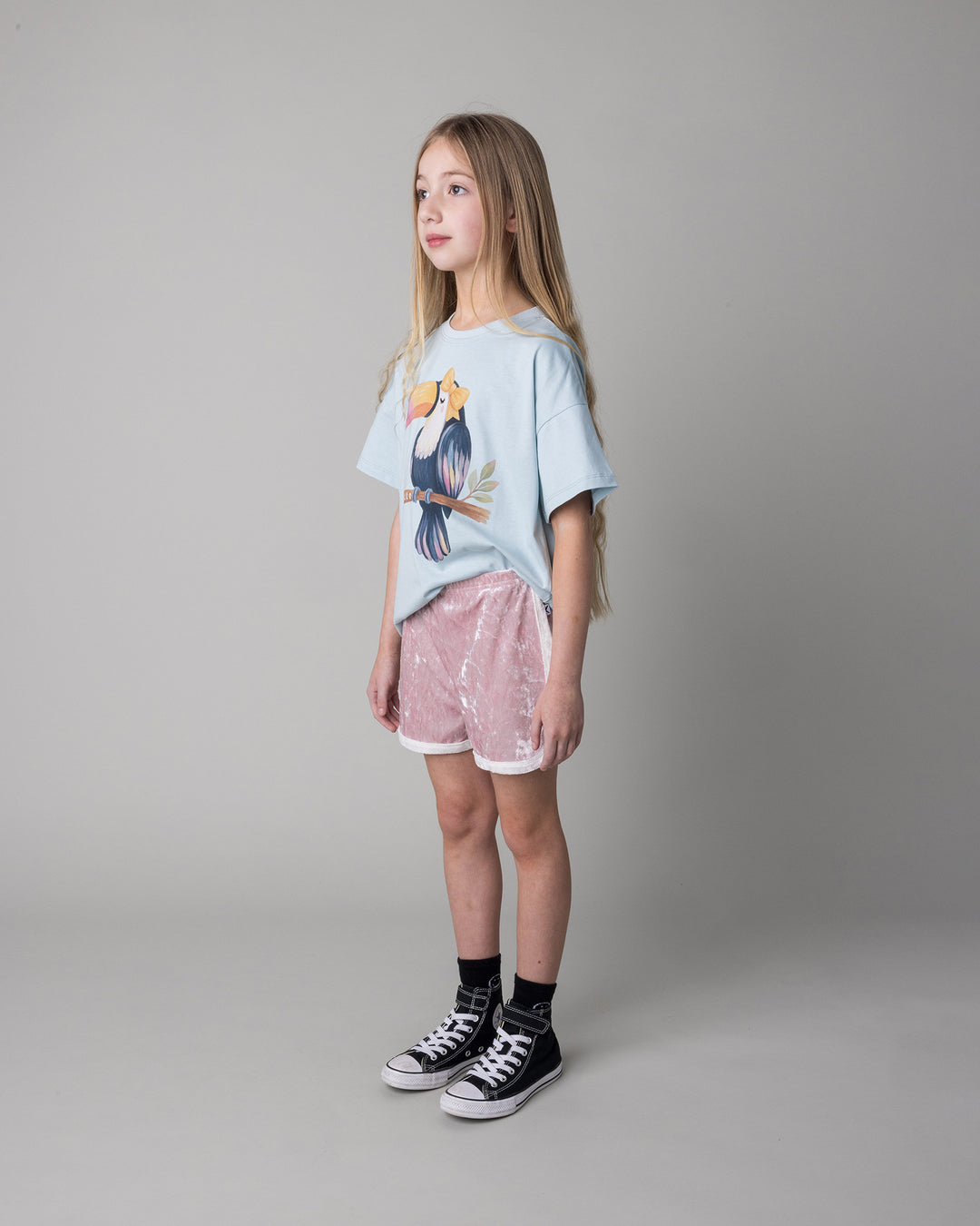 Kid wearing the Hello Toucan Tee in light blue with the Velvet Runner Short in blush and cream, side view