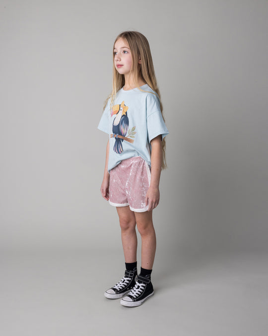 Kid wearing the Hello Toucan Tee in light blue with the Velvet Runner Short in blush and cream, side view