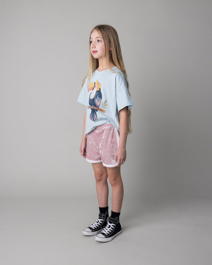 Kid wearing the Hello Toucan Tee in light blue with the Velvet Runner Short in blush and cream, side view