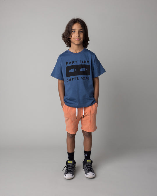 Kid wearing the Part Time Super Hero Tee in midnight with the Blasted Panel Short in orange wash, front view