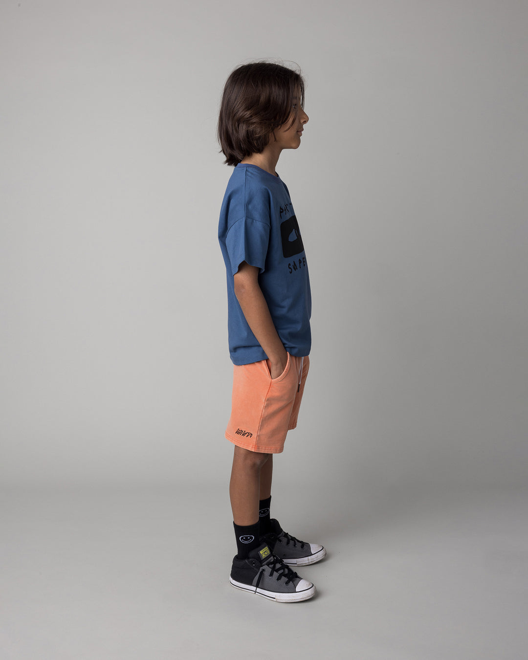 Kid wearing the Part Time Super Hero Tee in midnight with the Blasted Panel Short in orange wash, side view