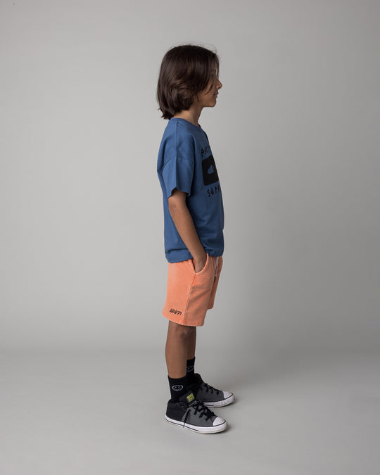 Kid wearing the Part Time Super Hero Tee in midnight with the Blasted Panel Short in orange wash, side view