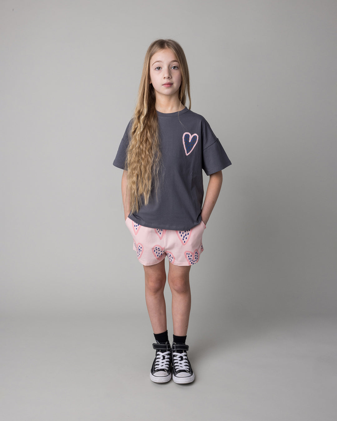 Kid wearing the Speckle Heart Tee in dark grey with the Speckle Heart Short in pink, front view