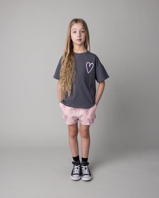 Kid wearing the Speckle Heart Tee in dark grey with the Speckle Heart Short in pink, front view