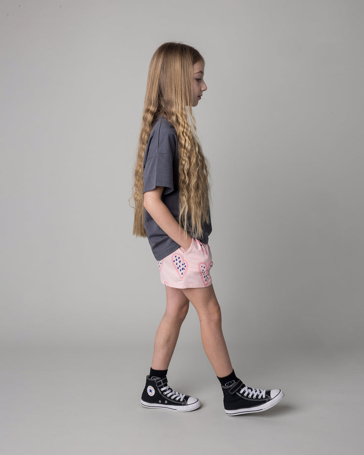 Kid wearing the Speckle Heart Tee in dark grey with the Speckle Heart Short in pink, side view