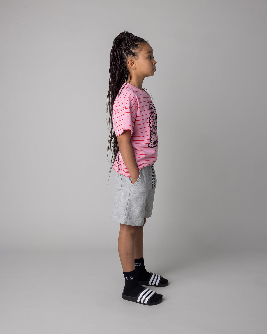Kid wearing the Smile Short in grey marle with the Happy Rainbow Tee in pink and red stripe, side view