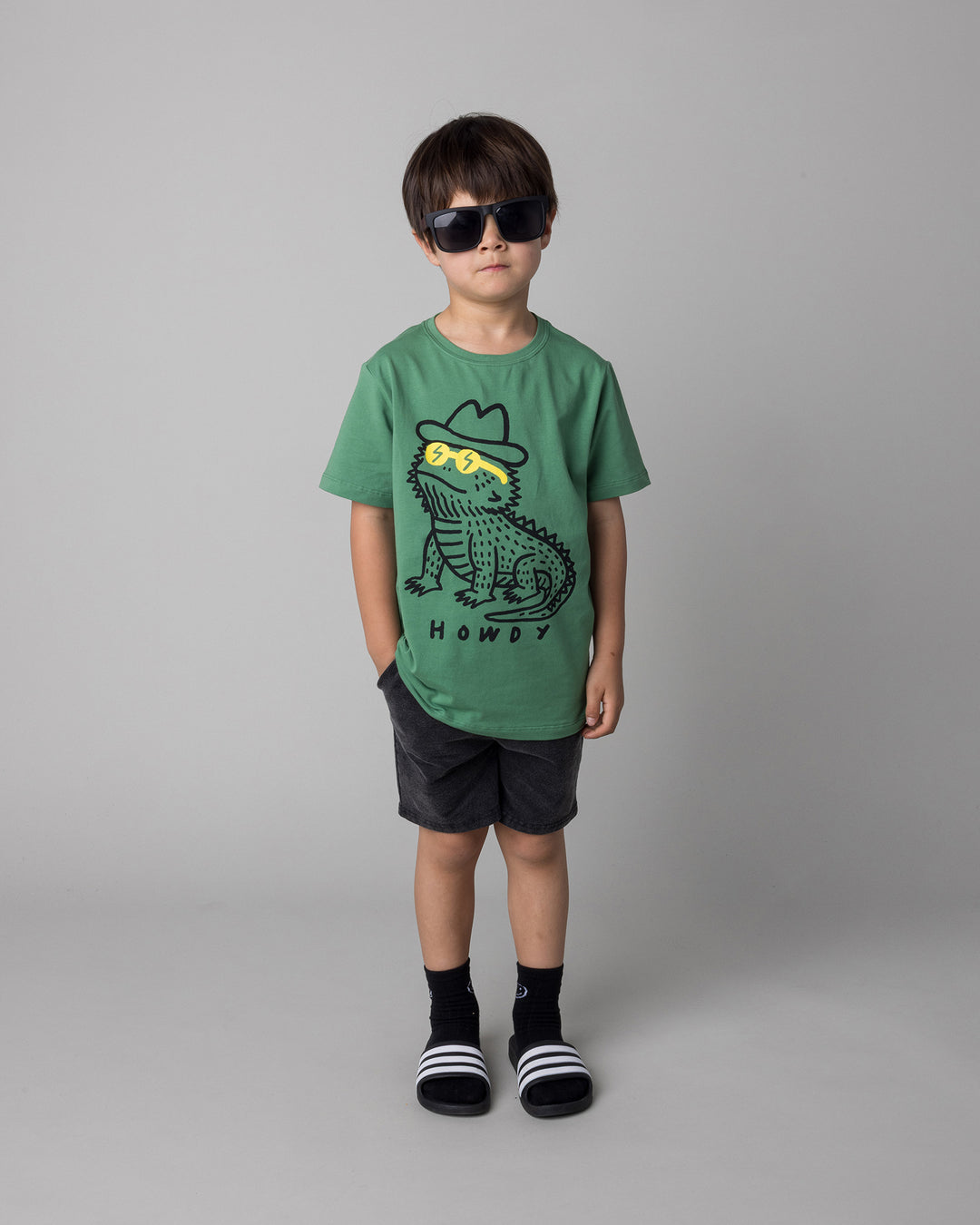 Kid wearing the Howdy Lizard Tee in turf with the Blasted Panel Short in black wash, front view