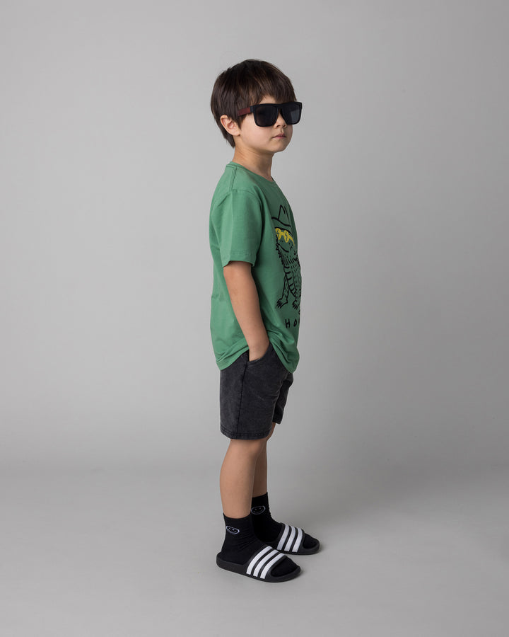 Kid wearing the Howdy Lizard Tee in turf with the Blasted Panel Short in black wash, side view