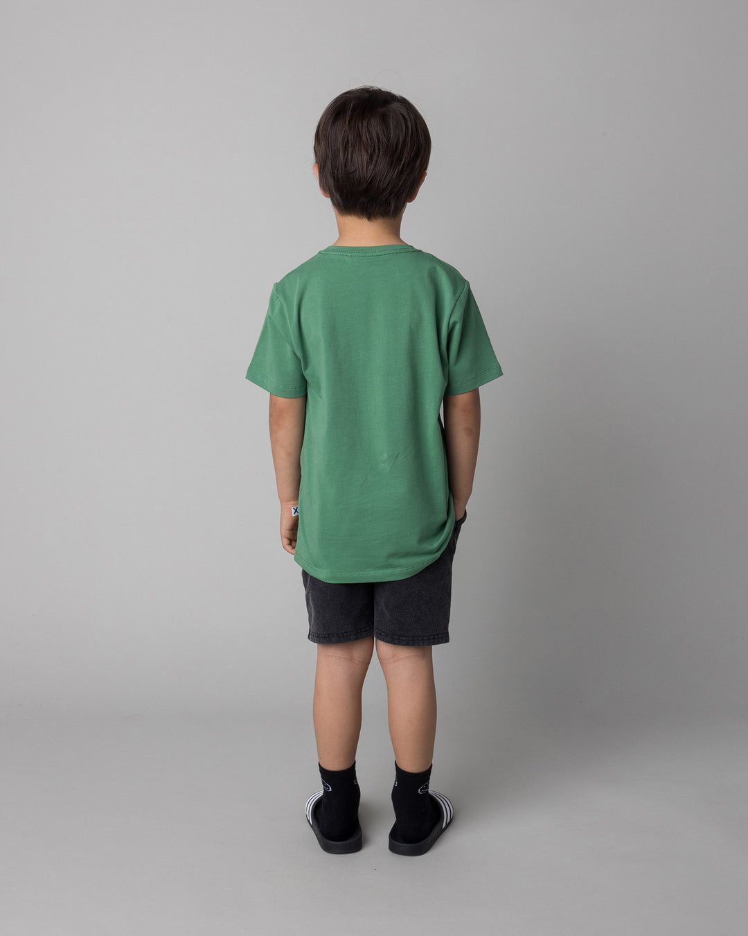Kid wearing the Howdy Lizard Tee in turf with the Blasted Panel Short in black wash, back view