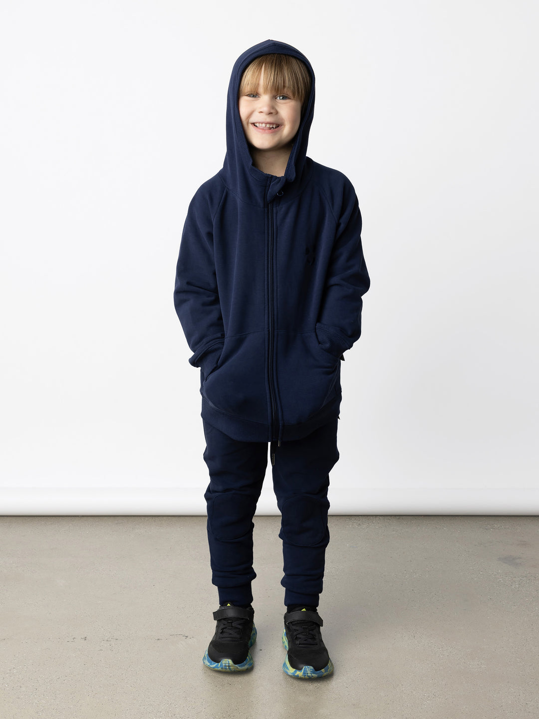 Minti kids clothing. Cosy zip through hoodie with kangaroo pockets for extra warmth! 2x2 rib trim on the hood, cuffs and hem. Small tonal Happy Face embroidery on the front. 330 Gram // Brushed Inside // 95% Cotton // 5% Elastane.