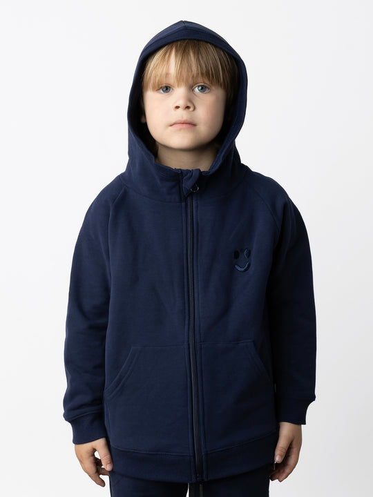 Minti kids clothing. Cosy zip through hoodie with kangaroo pockets for extra warmth! 2x2 rib trim on the hood, cuffs and hem. Small tonal Happy Face embroidery on the front. 330 Gram // Brushed Inside // 95% Cotton // 5% Elastane.