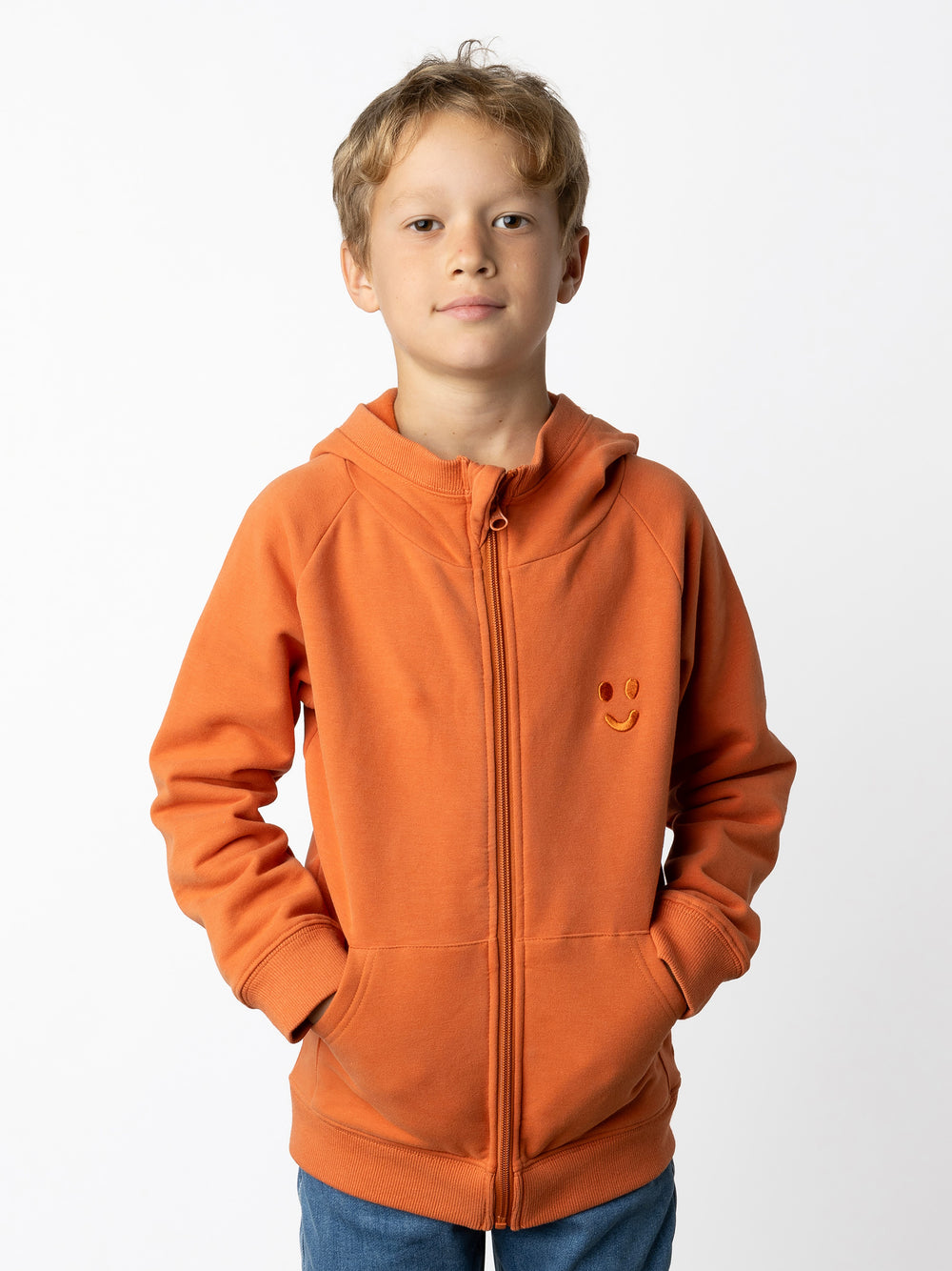 Minti kids clothing. Cosy zip through hoodie with kangaroo pockets for extra warmth! 2x2 rib trim on the hood, cuffs and hem. Small tonal Happy Face embroidery on the front. 330 Gram // Brushed Inside // 95% Cotton // 5% Elastane.