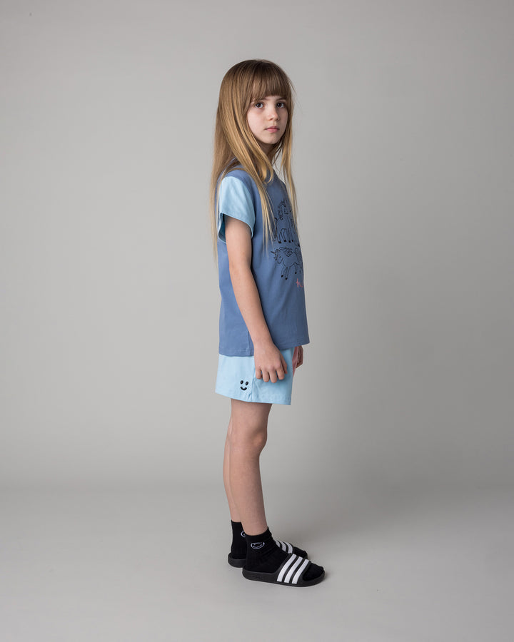 Kid wearing the Hello Unicorns Tee in mid blue and light blue and pink with the Two Tone Short in light blue and pink, side view