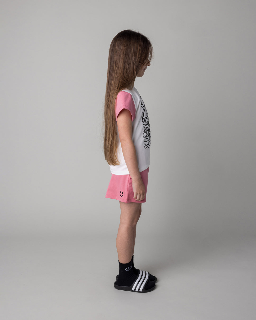Kid wearing the Messy Bows Tee in white and pinks with the Two Tone Short in pinks, side view